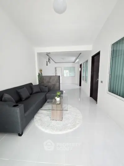 Modern living room with sleek gray sofa and glass coffee table on white tiled floor.