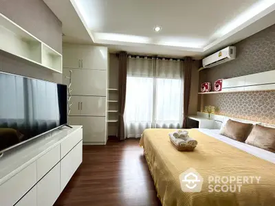 Modern bedroom with large TV and stylish decor, featuring a cozy bed and ample natural light.