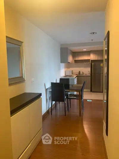 Modern apartment interior with open kitchen and dining area, featuring sleek furniture and wooden flooring.