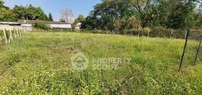 Spacious green plot of land with potential for development, surrounded by lush trees and clear skies.