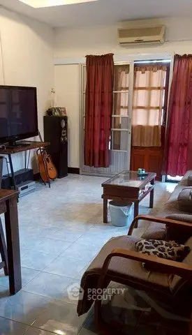 Cozy living room with natural light, featuring a TV, guitar, and comfortable seating.