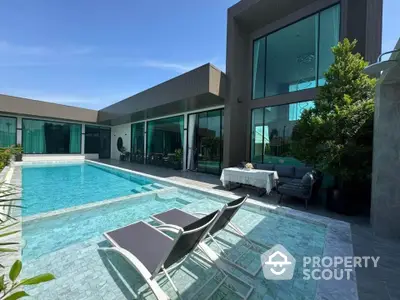 Luxurious modern villa with private pool and spacious outdoor seating area under clear blue sky.