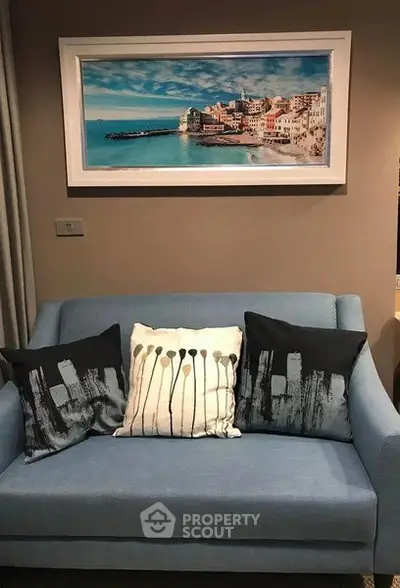 Cozy living room with stylish blue sofa and artistic cushions under a scenic framed wall art.
