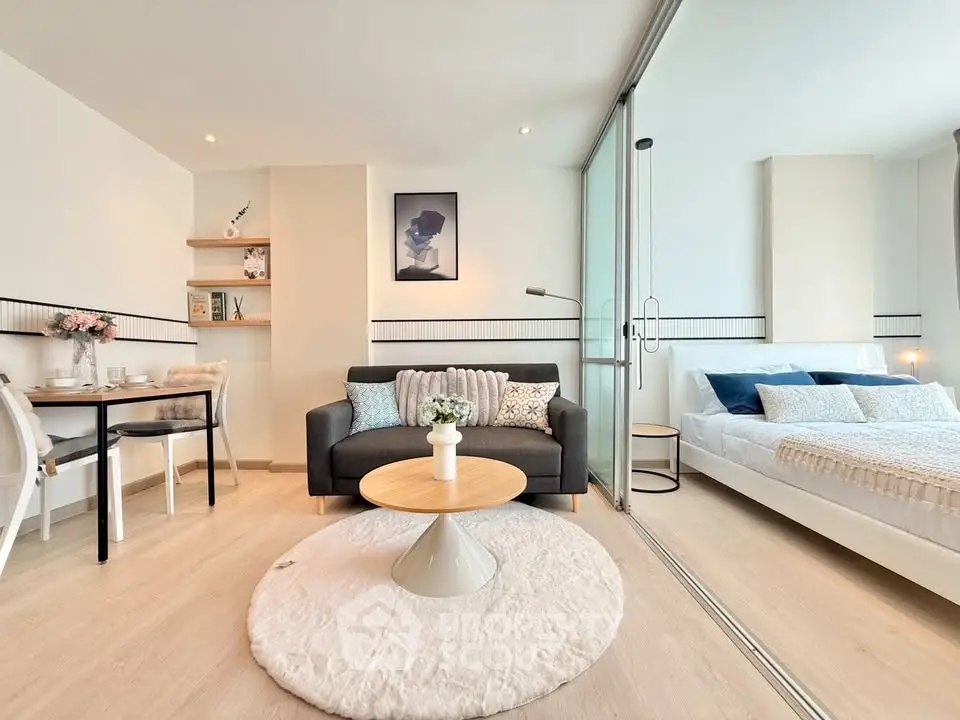 Modern open-plan living room with cozy bedroom separated by glass wall, featuring stylish decor and natural light.