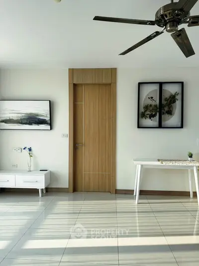 Modern living room with stylish decor and ceiling fan, featuring sleek furniture and wall art.