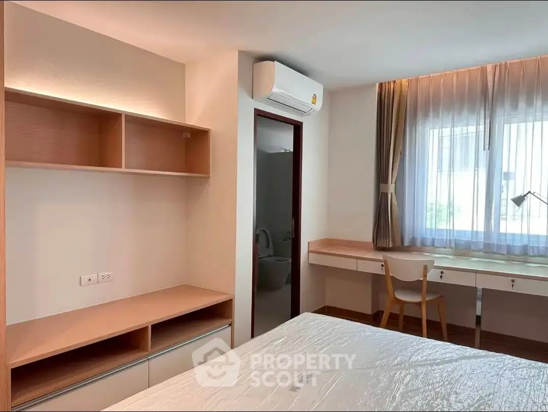Modern bedroom with built-in shelves and desk, featuring natural light and air conditioning.