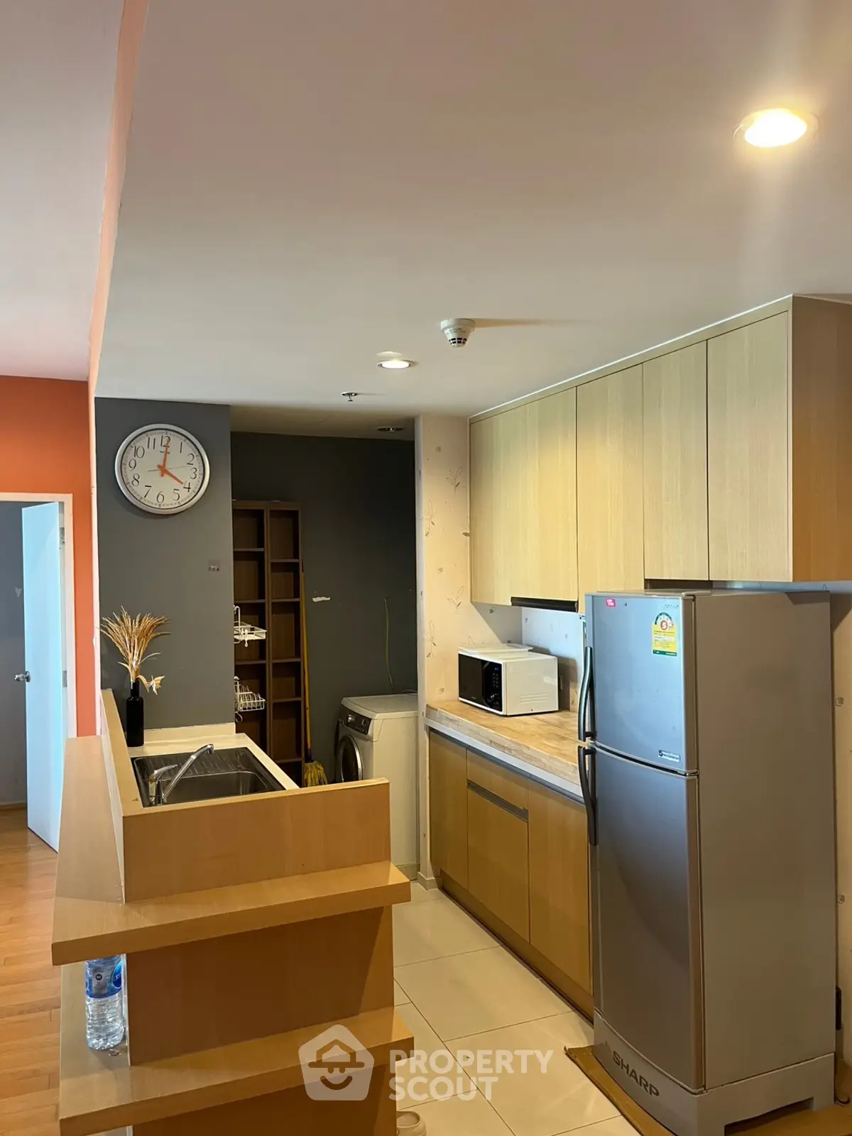 Modern kitchen with sleek cabinets, stainless steel fridge, and washing machine in a cozy apartment.