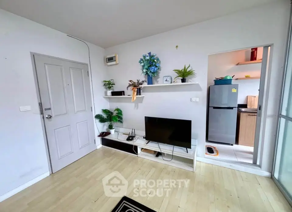 Modern living room with wooden flooring, TV setup, and adjacent kitchen area in a cozy apartment.