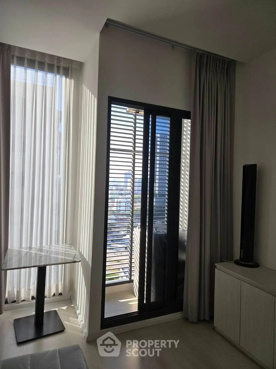 Modern living room with floor-to-ceiling windows and balcony view in urban apartment.