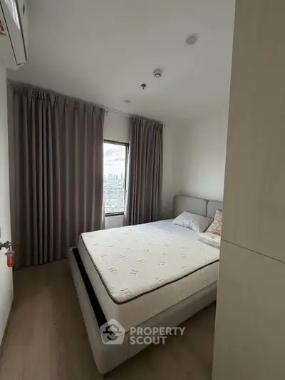 Modern bedroom with city view, featuring a comfortable bed and elegant curtains.