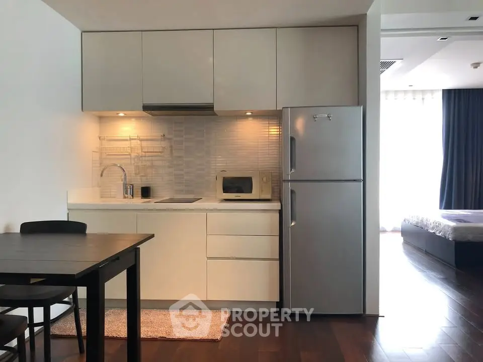 Modern kitchen with sleek cabinetry and stainless steel fridge in open-plan apartment.