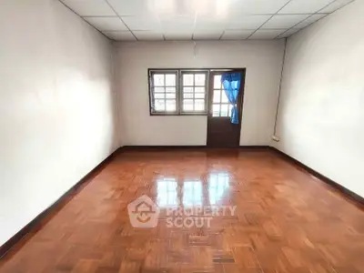 Spacious empty room with wooden flooring and natural light from window.