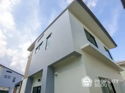 Modern two-story house with sleek design and large windows under a clear blue sky.