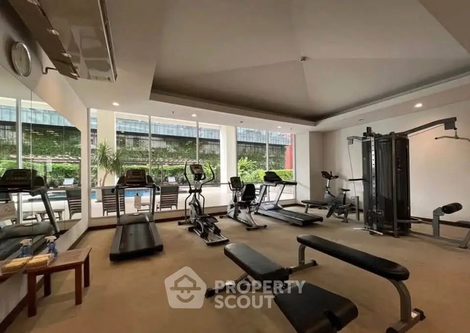 Spacious gym with modern equipment and pool view in luxury apartment complex.
