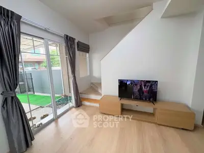 Modern living room with TV, wooden flooring, and sliding glass doors to garden.