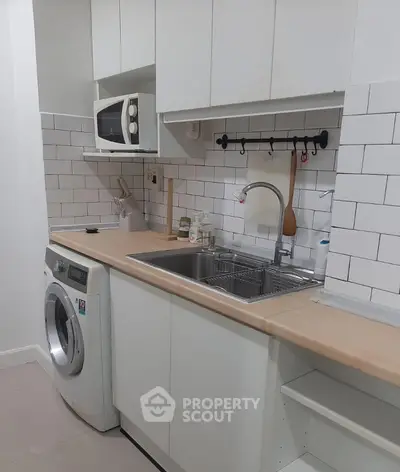 Modern kitchen with white cabinets, washing machine, and microwave, featuring a sleek subway tile backsplash.