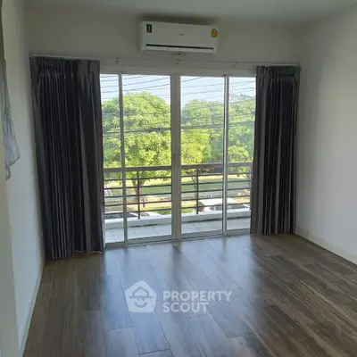 Spacious room with large windows and wooden flooring, offering a serene view of greenery.