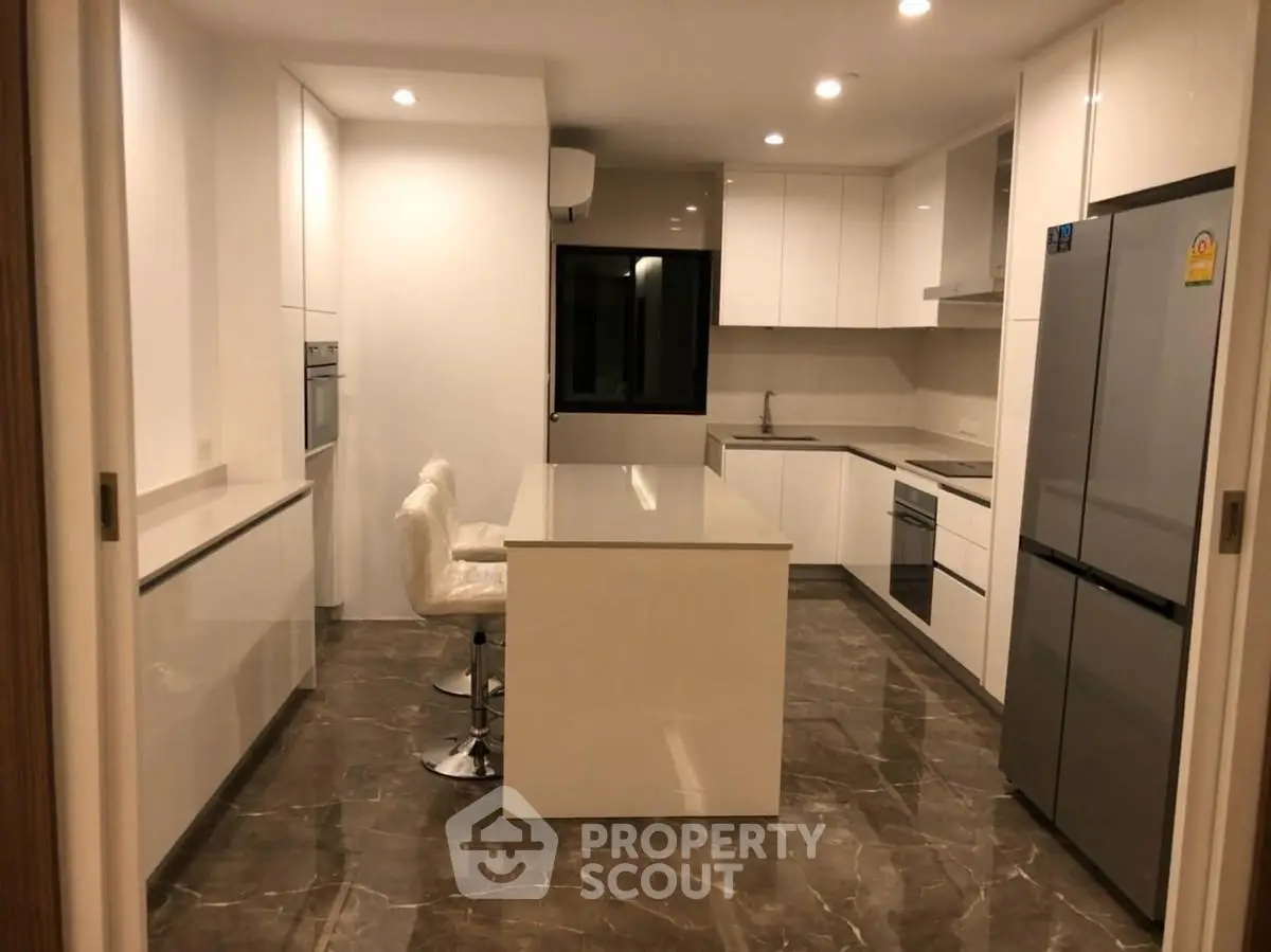 Modern kitchen with sleek white cabinetry and island, featuring built-in oven and spacious fridge.