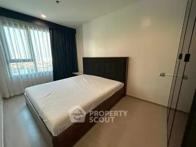 Spacious bedroom with large window and modern furnishings in a well-lit apartment.