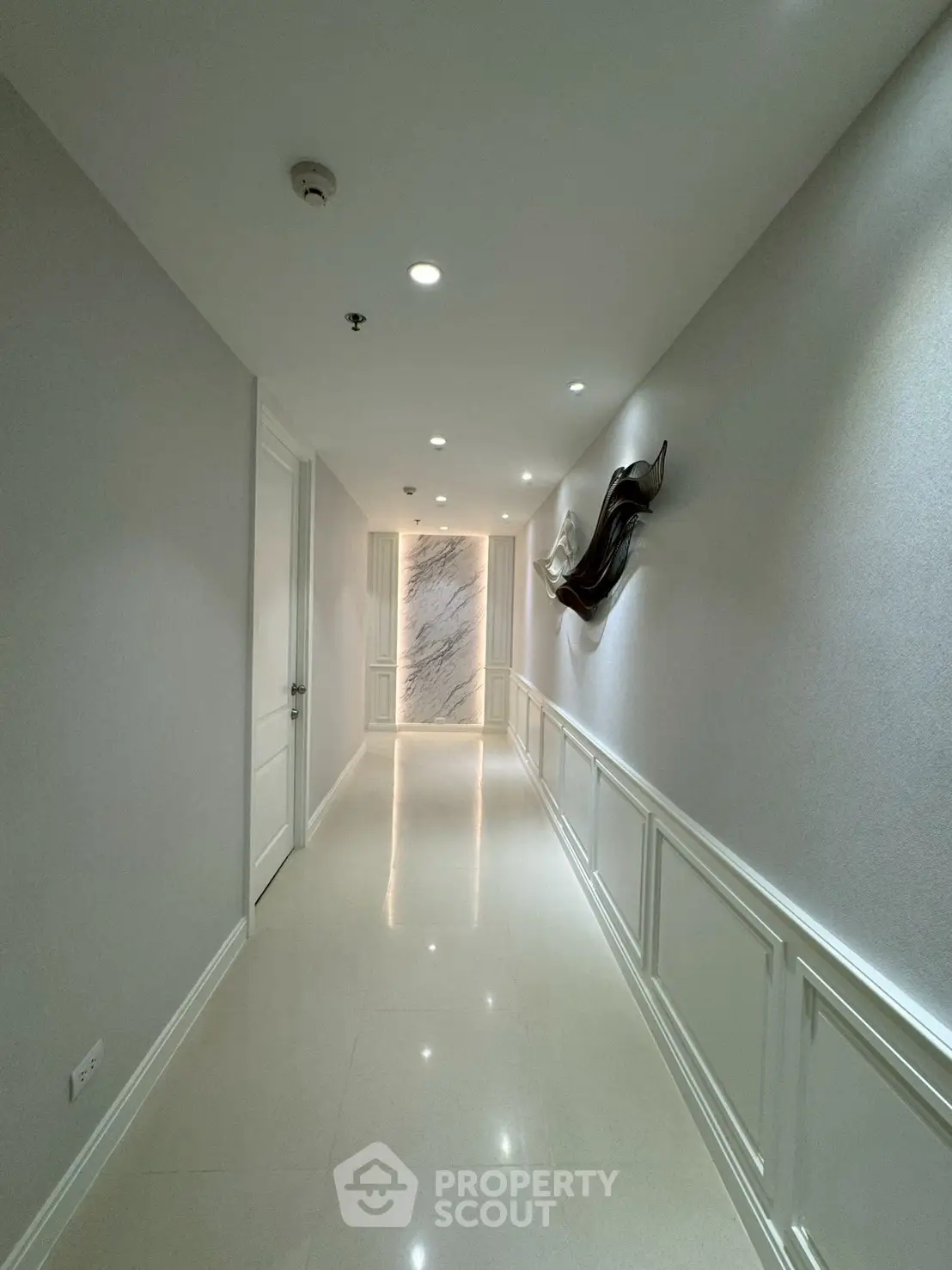 Elegant corridor with modern wall art and marble accent wall in luxury building.