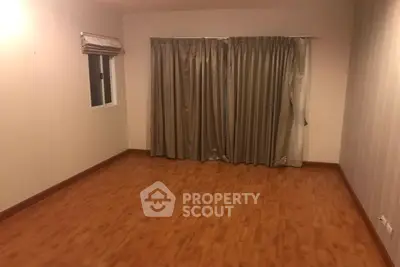 Spacious empty room with wooden flooring and large window draped with curtains.