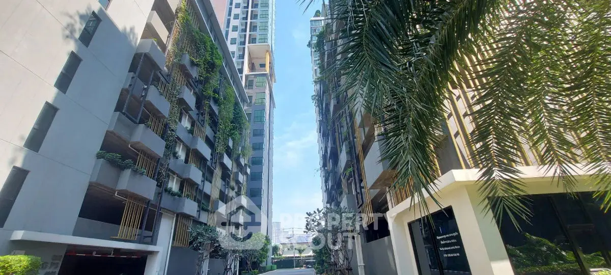 Modern urban apartment buildings with lush greenery and clear blue sky.