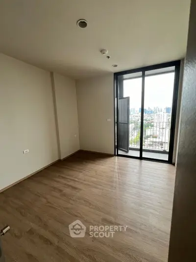 Spacious empty room with wooden flooring and city view balcony.