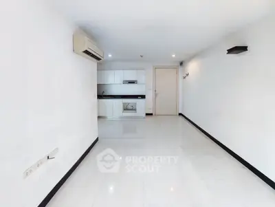 Spacious minimalist living room with sleek white tiles and modern kitchen area.
