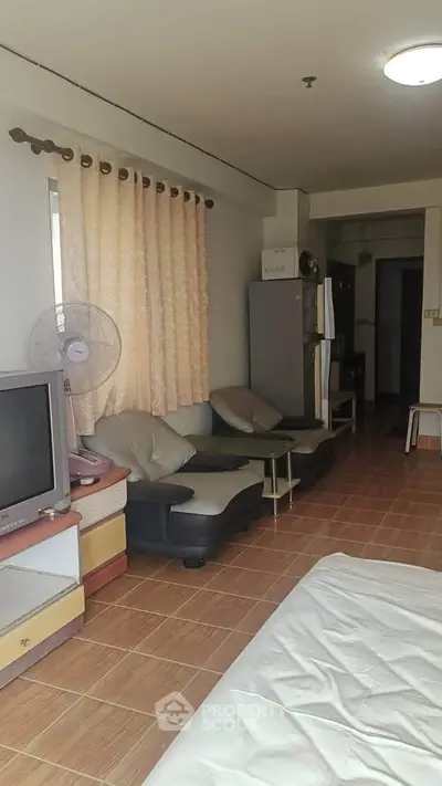 Cozy living room with TV, sofa, and fan in a well-lit apartment.
