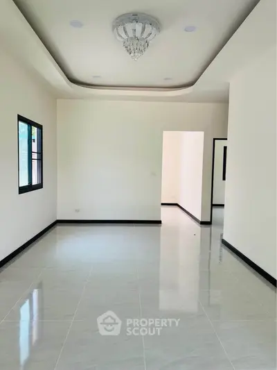 Spacious unfurnished living room with elegant ceiling light and large windows.