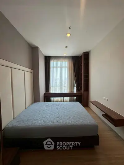 Spacious bedroom with large window and modern furnishings in a high-rise apartment.