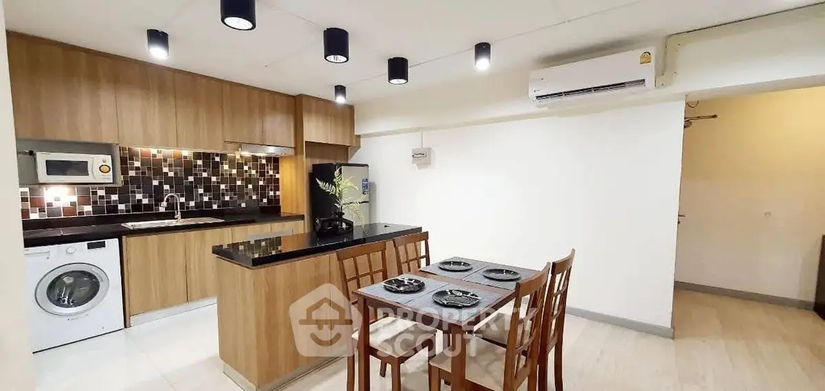 Modern kitchen with wooden cabinets, black countertop, and dining area in open layout.