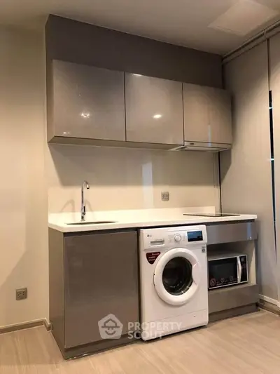 Modern kitchen with sleek cabinets, washing machine, and microwave in a compact layout.