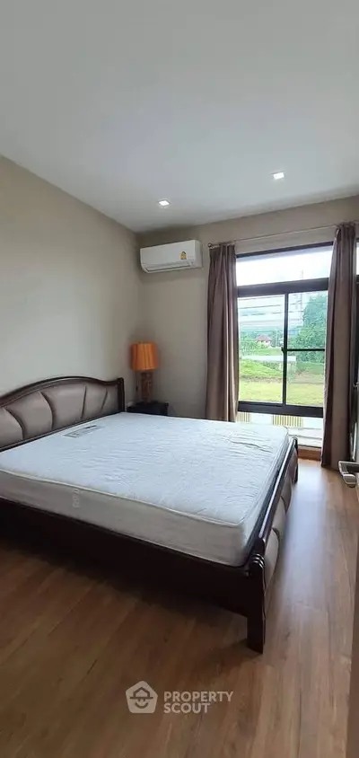 Spacious bedroom with large window and modern furnishings in a stylish apartment.
