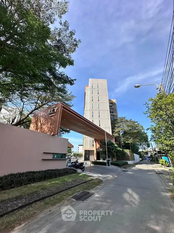 Modern high-rise building entrance with lush greenery and clear blue sky.