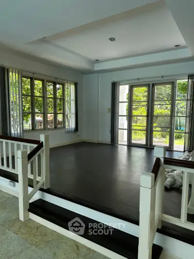 Spacious living room with large windows and garden view, featuring elegant flooring and natural light.