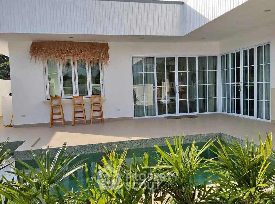 Modern villa with private pool and lush greenery, featuring large glass doors and a stylish outdoor bar area.