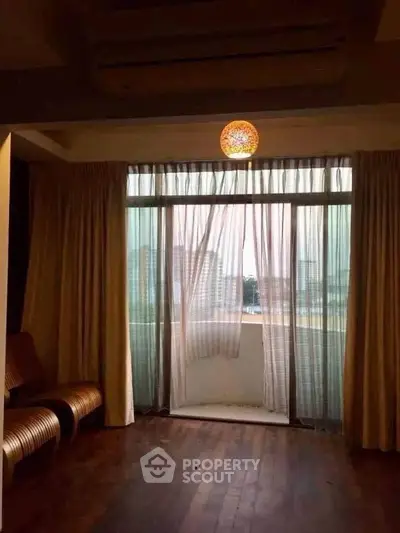 Spacious living room with large windows and balcony offering city views, perfect for relaxation.