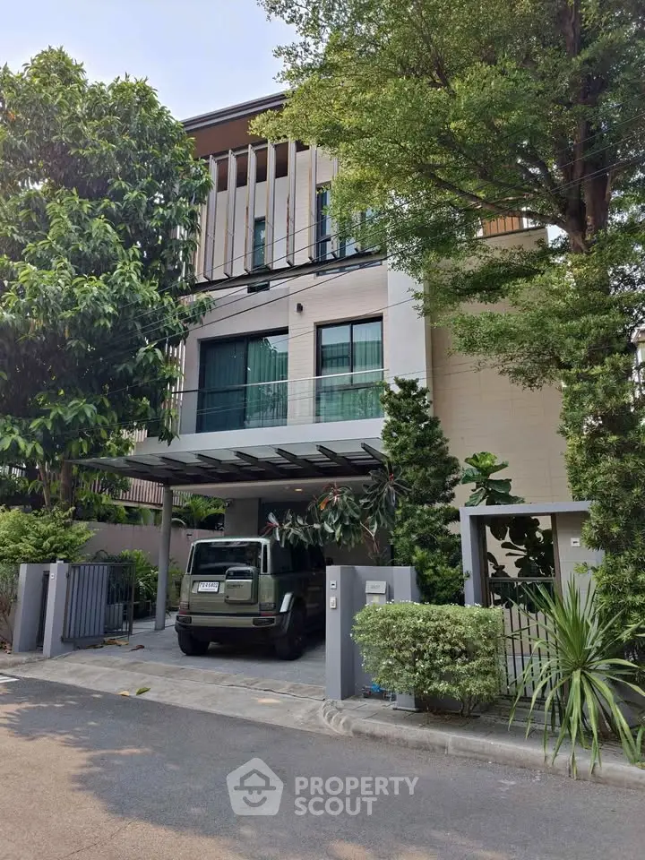 Modern three-story house with lush greenery and a sleek carport in a serene neighborhood.