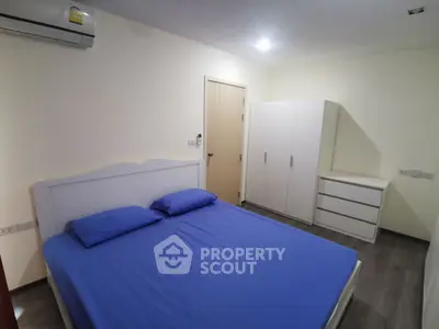 Modern bedroom with blue bedding, white furniture, and air conditioning unit.