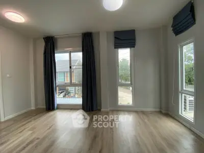 Spacious empty living room with large windows and elegant curtains, offering a bright and airy atmosphere.