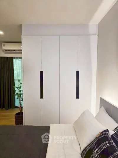 Modern bedroom with sleek white wardrobe and cozy bedding, featuring natural light and stylish decor.