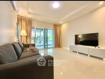 Spacious living room with modern decor and large TV, opening to a bright balcony.