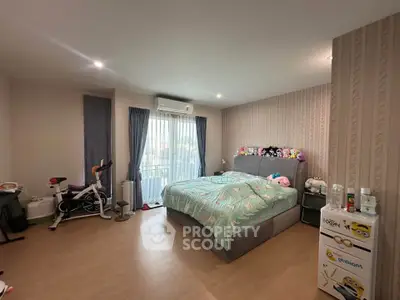 Spacious bedroom with modern decor and natural light, featuring a cozy bed and exercise bike.