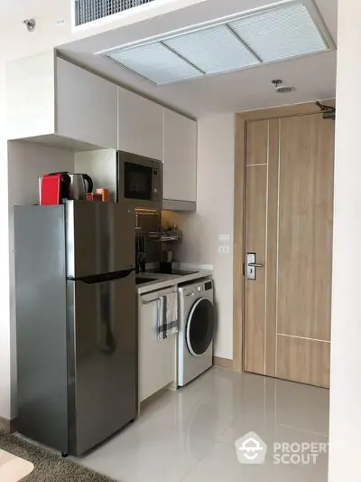 Modern compact kitchen with fridge, microwave, and washing machine in stylish apartment.