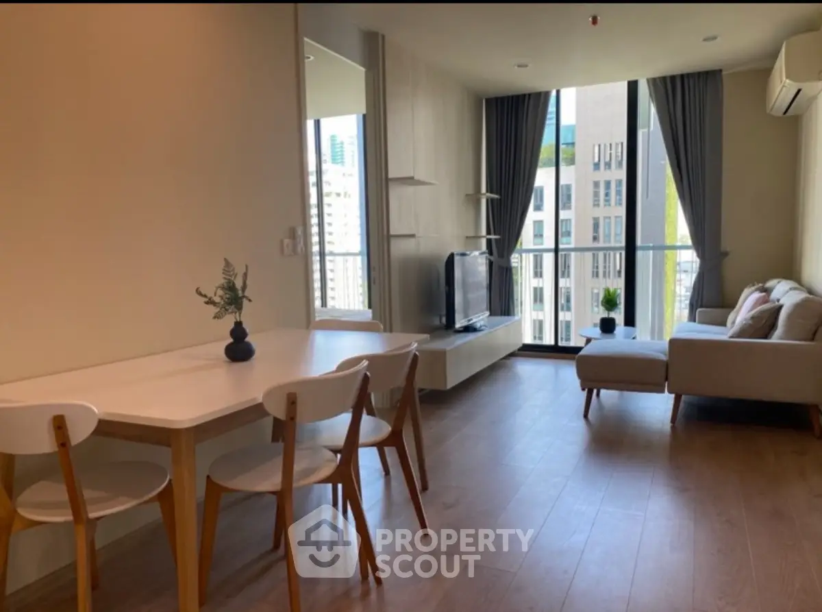Modern living room with dining area and city view, featuring sleek furniture and large windows.