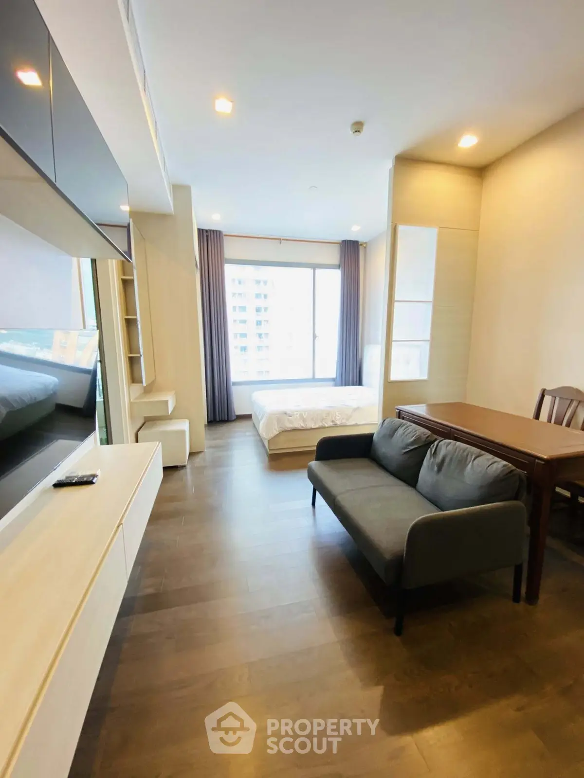 Modern studio apartment with open layout, featuring a cozy living area and large window for natural light.