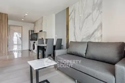 Modern living room with sleek gray sofa and marble accent wall in open-plan apartment.