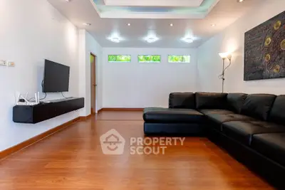 Spacious modern living room with sleek black sofa and wall-mounted TV, featuring elegant lighting and wooden flooring.