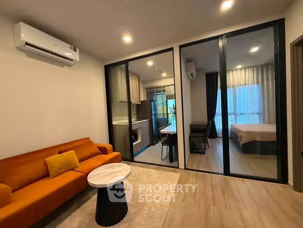 Modern living room with orange sofa and glass partition leading to bedroom, featuring sleek design and cozy ambiance.